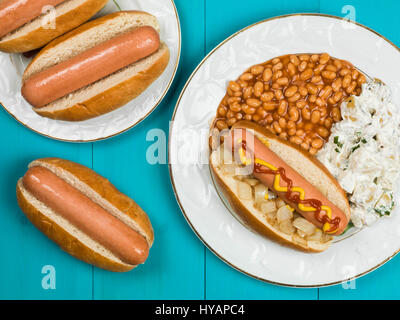 Hot Dog in einem Brötchen mit Baked Beans und Kartoffelsalat auf blauem Grund Stockfoto