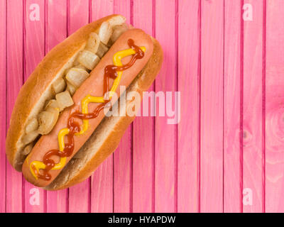 Hot Dog in einem Brötchen mit gebratene Zwiebel Ketchup und Senf vor einem rosa Hintergrund Stockfoto