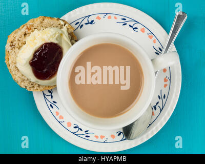 Tasse Tee oder Kaffee mit Scones, Clotted Cream und Erdbeermarmelade auf blauem Grund Stockfoto