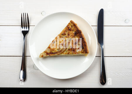 Stück Kuchen auf einem Teller mit Messer und Gabel auf einem weißen Holztisch. Ansicht von oben Stockfoto