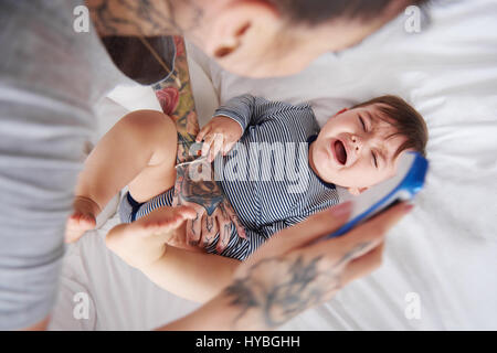 Armes Baby weint während Mami das Fieber messen Stockfoto