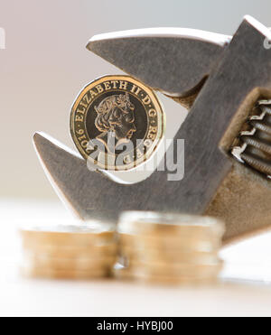 Ein Pfund £1 Münze in einen verstellbaren Schraubenschlüssel statt vor einem hellen Hintergrund mit Münzen gestapelt im Vordergrund zeigt eine Pressung auf Finanzen Stockfoto