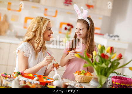 Junge Mutter in der Küche mit Mädchen bemalen von Ostereiern Stockfoto