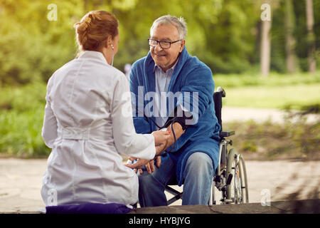 Krankenschwester, die Überprüfung der Hypertonie-Beurteilung der Blutdruck älterer Mann im Rollstuhl Stockfoto