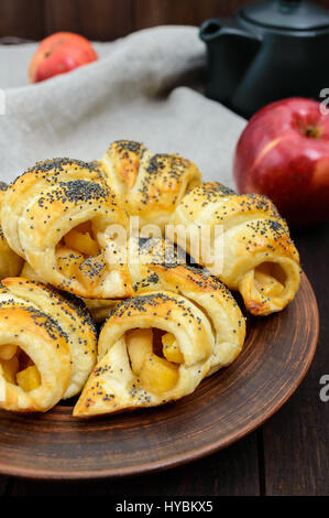 Hausgemachte Croissants (Brötchen) mit Äpfeln, dekoriert mit Mohn in einer Ton-Schüssel auf einem dunklen Hintergrund aus Holz. Nahaufnahme Stockfoto