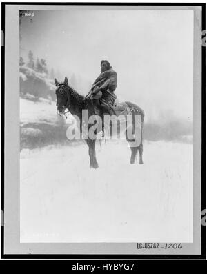 Edward S. Curtis’ Foto „The Scout in Winter, Crow“ aus dem Jahr 1908 zeigt einen Crow-Indianer-Scout in der verschneiten Landschaft des amerikanischen Westens. Das Stück veranschaulicht Curtis’ Engagement, das Leben der amerikanischen Ureinwohner um die Jahrhundertwende zu dokumentieren. Stockfoto