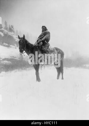 „The Scout in Winter, Crow“ von Edward S. Curtis, aufgenommen im Jahr 1908, fängt einen Indianer der Krähe in Winterkleidung ein. Dieses restaurierte Foto zeigt die kulturelle Bedeutung und die harten Winterbedingungen, denen die indigenen Völker während dieser Zeit gegenüberstanden. Stockfoto