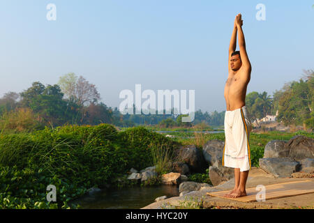 Indischer Mann neben einem Fluss in Süd-Indien Yoga zu praktizieren. Stockfoto