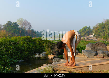 Indischer Mann neben einem Fluss in Süd-Indien Yoga zu praktizieren. Stockfoto