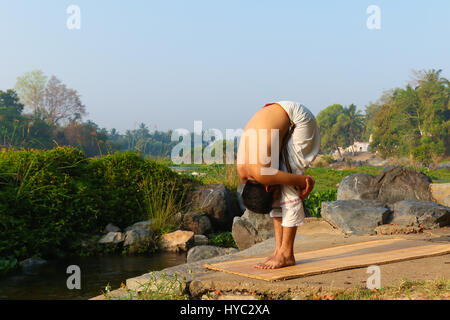 Indischer Mann neben einem Fluss in Süd-Indien Yoga zu praktizieren. Stockfoto