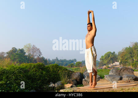 Indischer Mann neben einem Fluss in Süd-Indien Yoga zu praktizieren. Stockfoto