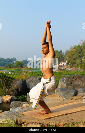 Indischer Mann neben einem Fluss in Süd-Indien Yoga zu praktizieren. Stockfoto