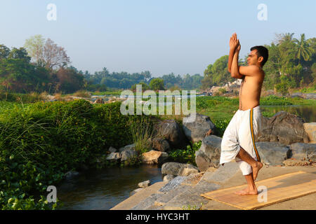 Indischer Mann neben einem Fluss in Süd-Indien Yoga zu praktizieren. Stockfoto