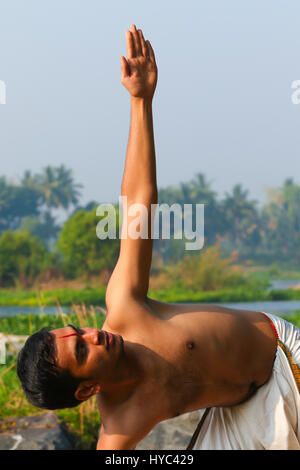 Indischer Mann neben einem Fluss in Süd-Indien Yoga zu praktizieren. Stockfoto