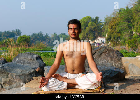 Indischer Mann neben einem Fluss in Süd-Indien Yoga zu praktizieren. Stockfoto