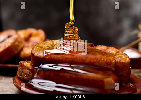 Honig fallen auf einige Torrijas, typisch spanische Dessert für Fastenzeit und Ostern, serviert in einem Tontopf Platte, auf einem rustikalen Holztisch Stockfoto