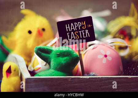 einige Küken gelb Spielzeug Spielzeug ein grünes Kaninchen, einige verzierte Eiern und ein schwarzer Schild mit dem Text Frohe Ostern Stockfoto