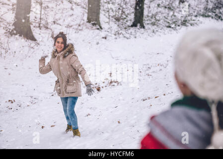 Mädchen werfen Schneeball im verschneiten Wald Stockfoto