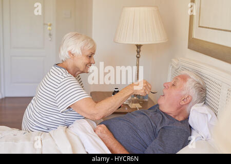 Ältere Frau, die Medizin zu ihrem kranken Mann im Bett zu geben Stockfoto