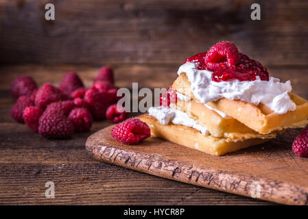 Belgische Waffeln mit Himbeeren, Bananen und Sahne auf rustikalen Tisch. Stockfoto