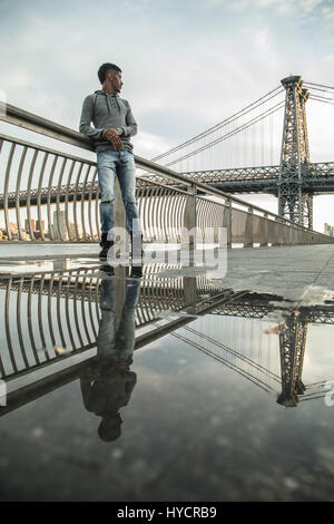 Ein junger Mann sitzt und den Blick auf New Yorks Williamsburg Brücke bewundert. Im Herbst 2016 in Brooklyn, New York City gedreht. Stockfoto