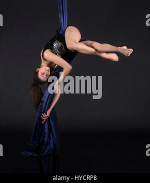 Die junge, lächelnde Frau macht Übungen auf den Leinwänden. Studioaufnahme der Performance auf dunklem Hintergrund. Stockfoto