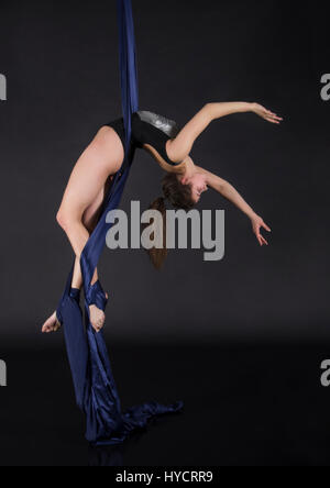 Die junge, lächelnde Frau macht Übungen auf den Leinwänden. Studioaufnahme der Performance auf dunklem Hintergrund. Stockfoto