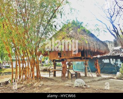 thatched Dach Hütte mit Holzschnitzereien darunter mit langen Bambusstämmen auf seiner Seite Stockfoto