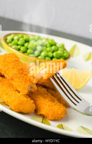 Fischstäbchen auf einem Teller mit einer Schüssel mit Erbsen und einer Scheibe Zitrone Stockfoto