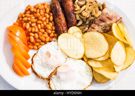 Volles englisches Frühstück mit Würstchen, Tomaten und Champignons, Ei, Speck, gebackene Bohnen und chips. Stockfoto