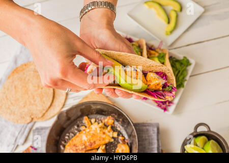 Frau, die Tortilla mit Tilapia, Avocado und Rotkohl vorbereitet Stockfoto