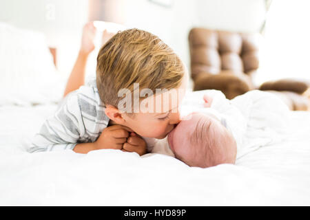 Bruder (4-5) auf dem Bett liegend und küssende Schwester (0-1 Monate) Stockfoto