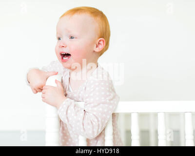 Kleines Mädchen ( 12-17 Monate) Mit roten Haaren in der Krippe stehend Stockfoto