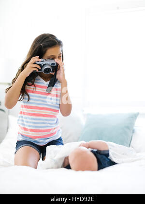 Mädchen (10-11) fotografiert ihren kleinen Bruder (12-17 Monate) Liegen auf dem Bett Stockfoto