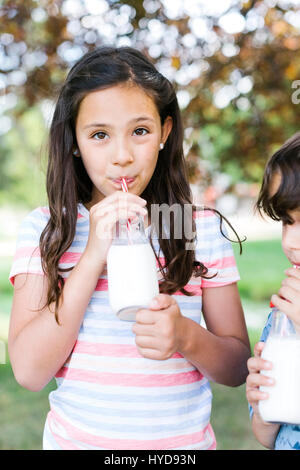 Mädchen (10-11) und Jungen (6-7) im Park trinken Milch Stockfoto