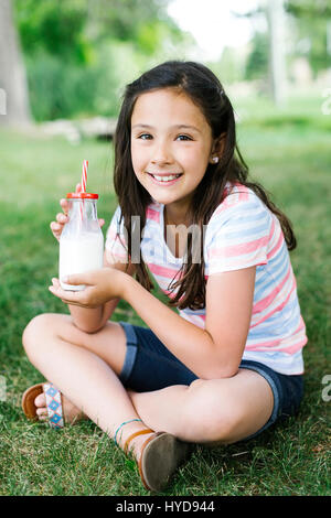 Mädchen (10-11) sitzt auf Gras mit einem Glas Milch Stockfoto