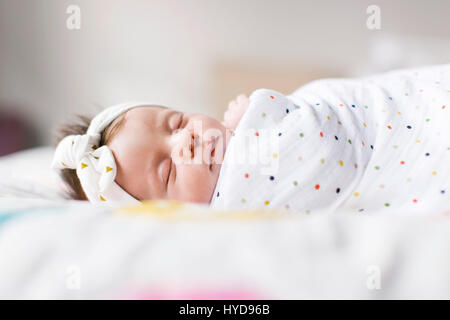 Baby girl (0-1 months) wrapped in blanket sleeping on bed Stockfoto