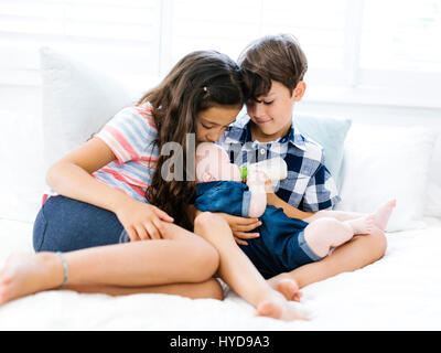 Drei Geschwister (6-11 Monate, 6-7, 10-11) sitzen zusammen auf dem Bett Stockfoto