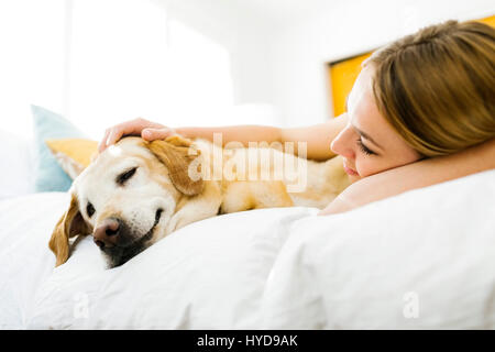 Junge Frau streichelte golden Retriever im Bett Stockfoto
