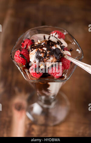 Eisbecher im Vintage Glas mit Schokoladensauce, Nüssen und Himbeeren Stockfoto