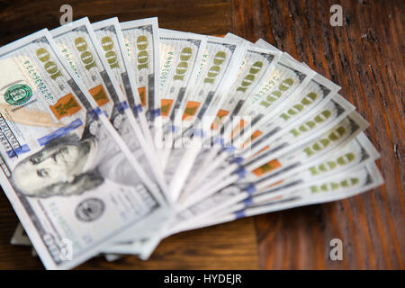 Ein Stapel von ganz neuen Hundert-Euro-Scheine in US-Währung schwärmten aus, auf einem dunkelbraunen hölzernen Tisch Stockfoto