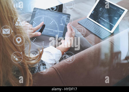 Brünette Frau mit digitalen Talet und Laptop-Computer auf Sofa im Wohnzimmer mit virtuellen Schnittstelle grafische Symbole Netzwerkdiagramm Stockfoto