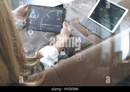 Brünette Frau mit digitalen Talet und Laptop-Computer auf Sofa im Wohnzimmer mit virtuellen Schnittstelle grafische Symbole Netzwerkdiagramm Stockfoto