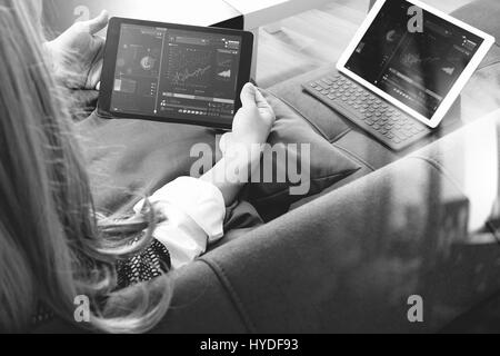 Brünette Frau mit digitalen Talet und Laptop-Computer auf Sofa im Wohnzimmer, schwarz / weiß Stockfoto