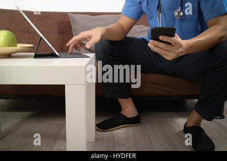 Medizin und Gesundheit Zusammenhang Arzt Hand arbeiten mit smart-Phone, digitale Tablet-Computer, Stethoskop, sitzen auf dem Sofa im Wohnzimmer Stockfoto