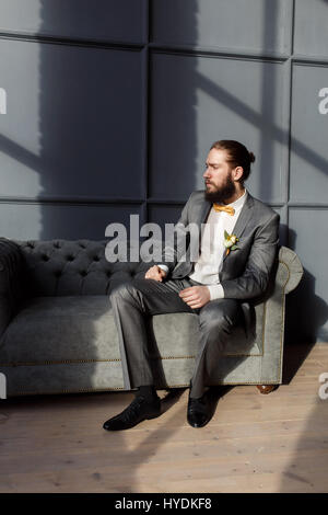Schön stark, brutale bärtiger Mann sitzt auf dem grauen Sofa im Zimmer Stockfoto