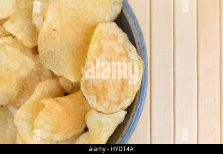 Enge Draufsicht eine alte Steingut-Schale gefüllt mit Salz und Essig gewürzt Kartoffelchips auf Holz Tischset. Stockfoto