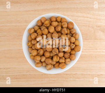 Draufsicht auf eine Portion geröstete Kichererbsen mit Meersalz in einer kleinen weißen Schüssel auf einem Holztisch. Stockfoto