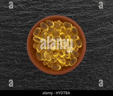 Draufsicht auf eine Schüssel mit Vitamin-A-Gel-Kapseln auf einem schwarzen Schiefer Tisch. Stockfoto