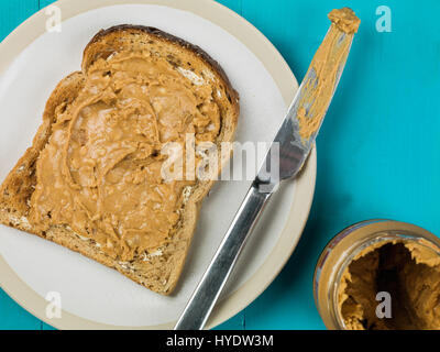 Crunchy Erdnussbutter zu verbreiten, auf Toast auf blauem Grund Stockfoto